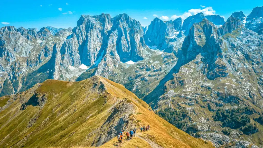 Hikers on a mountain ridge along the Peaks of the Balkans trail with dramatic peaks in the background